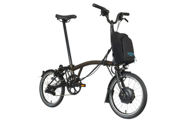 Un utilisateur plie son vélo brompton electric c line noir sur un trottoir urbain moderne devant une architecture contemporaine.