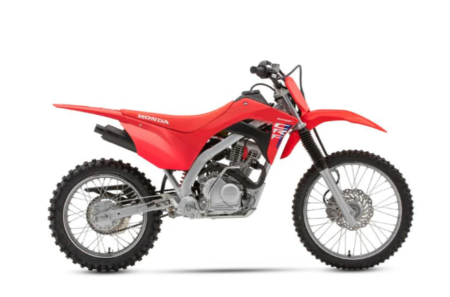 Moto honda crf125f rouge et blanche stationnée sur terrain tout-terrain pour pratique du motocross.