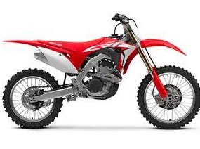 Moto honda crf250r rouge et noire stationnée sur un terrain de motocross.